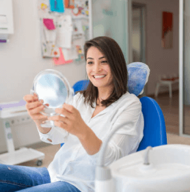 Woman holding dental mirror in modern dental office, smiling at camera