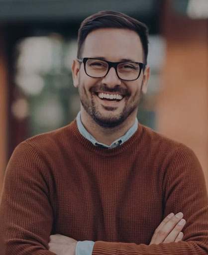 Smiling man with glasses wearing rust-colored sweater in dental office setting.