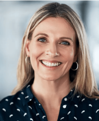 Professional headshot of smiling woman with blonde hair wearing polka dot blouse against blurred background.