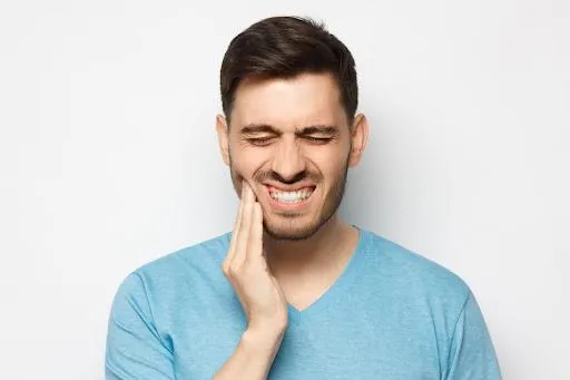 Man in blue shirt smiling with hand to face against white background.